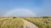 A fogbow arches over a sandy trail winding through tall beach grass near Manzanita, Oregon, on a misty coastal morning.