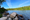 Rocky shoreline along Jordan Pond in Acadia National Park, with clear blue water, dense evergreen trees, and mountain slopes in the background.